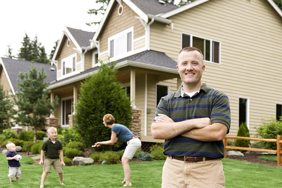 About Our Agency - Happy Couple Playing Outside With Their Two Boys in Front of New House